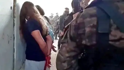 Hostages and Missing Families Forum Israeli hostage Naama Levy (L) is seen with her hands bound and facing a wall as Hamas gunmen stand next to her in the newly released video filmed by Hamas gunmen at Nahal Oz base on 7 October (22 May 2024)