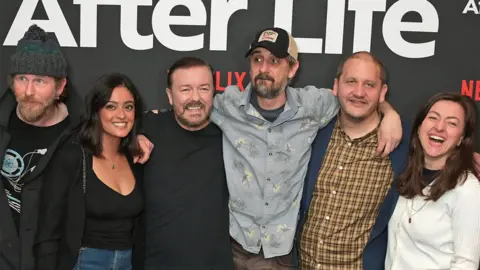 Getty Images The cast of After Life at a launch event. Left to right is a man, woman, man, man, man and woman. The background has Netflix branding.