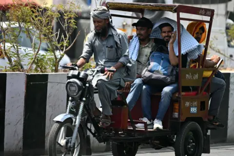 Getty Images People travelling on an electric rickshaw cover their heads during a hot sunny day in old quarters of Delhi on May 21, 2024. Indian authorities in the capital have ordered schools shut early for the summer holiday, after temperatures hit 47.4 degrees Celsius (117 degrees Fahrenheit) with Delhi gripped by a "severe heatwave". (Photo by Arun SANKAR / AFP) (Photo by ARUN SANKAR/AFP via Getty Images)