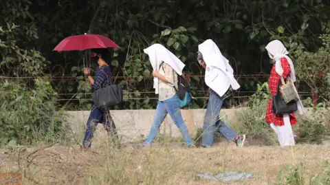 EPA-EFE/REX/Shutterstock Indian girls use their white jackets and umbrella to protect themselves from the sun during a heatwave near New Delhi, India, 22 May 2023. India Meteorological Department issued a heat wave warning after several parts of the Indian capital recorded maximum temperatures above 45 degrees Celsius. Heatwave warning issued for several parts of India, New Delhi - 22 May 2023