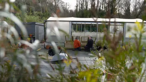 BBC/Gwyndaf Hughes Photograph of a greenhouse with two people kneeling in front of it