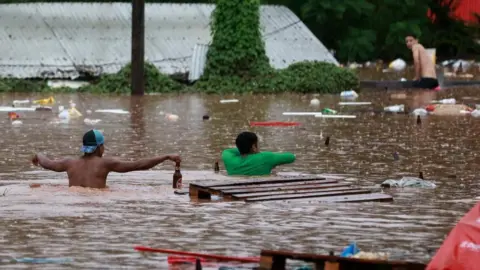 Reuters People walk in a flooded area next to the Taquari River during heavy rains in Encantado, Rio Grande do Sul state, Brazil, May 2, 2024.