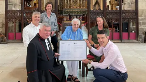 The Cotswold PR Company Lucille Terry being presented with a framed letter in a church