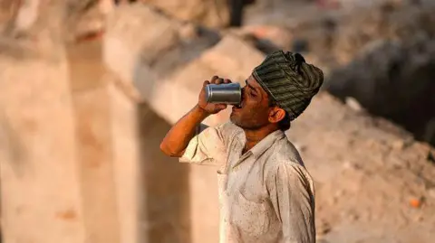 Getty Images A construction worker quenches his thirst as he takes a break, amid the ongoing intense heatwave on a hot summer day along the bank of the river Yamuna, in New Delhi.