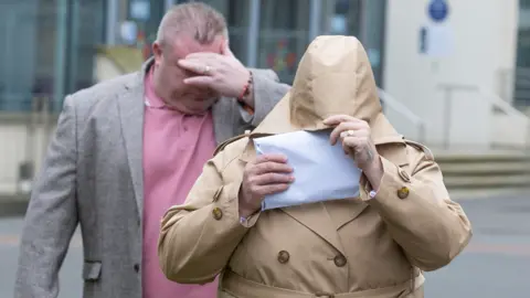 Gareth Everett/Huw Evans Agency Bernard Mcdonagh in a pink shirt and grey jacket covering his face stood behind Ann McDonagh who is wearing a beige coat with a letter covering her face