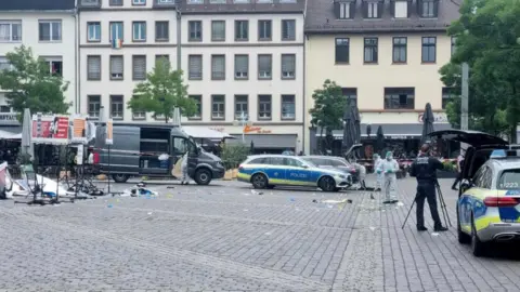 DPA via AP Debris on ground of market with microphone stands and police vehicles 