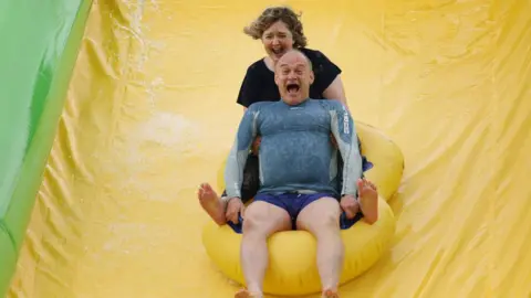 Getty Images Sir Ed Davey and Anna Sabine, parliamentary candidate for Frome and East Somerset, ride the Ultimate Slip 'n' Slide at Eastcote Farm during an election campaign visit in Beckington
