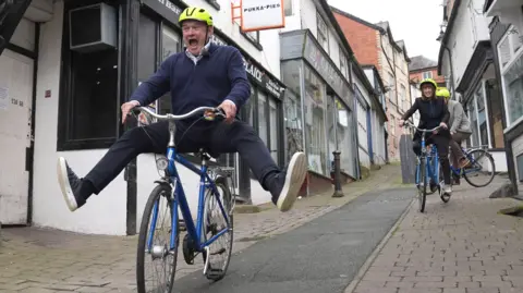 PA Media Liberal Democrat Leader Sir Ed Davey riding a bike during a visit to Knighton, Powys