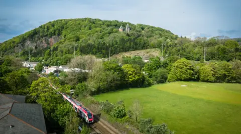 Transport for Wales A train travels on a train track surrounded by fields and trees