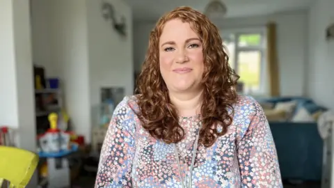 BBC Red haired woman sits at a table in her living room